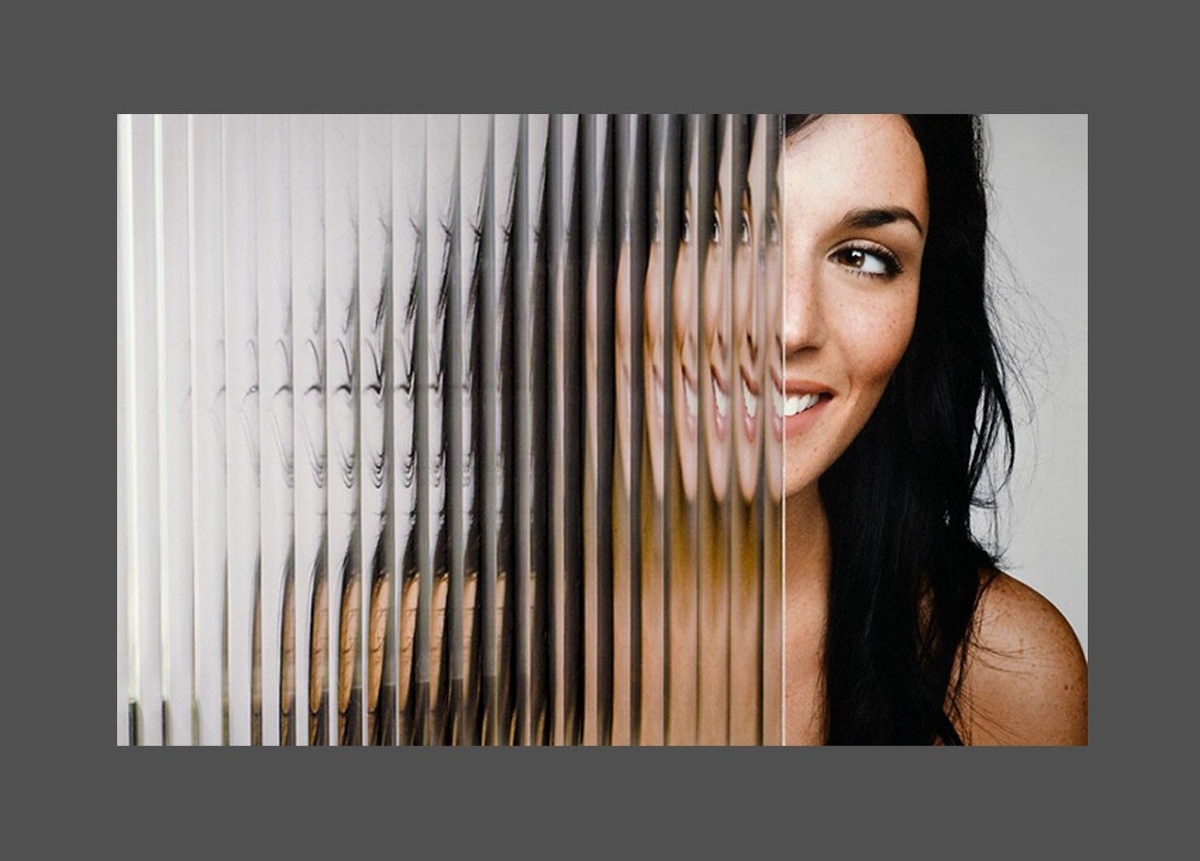 Smiling woman semi-shrouded by a accordian-like glass partition, distorting her image