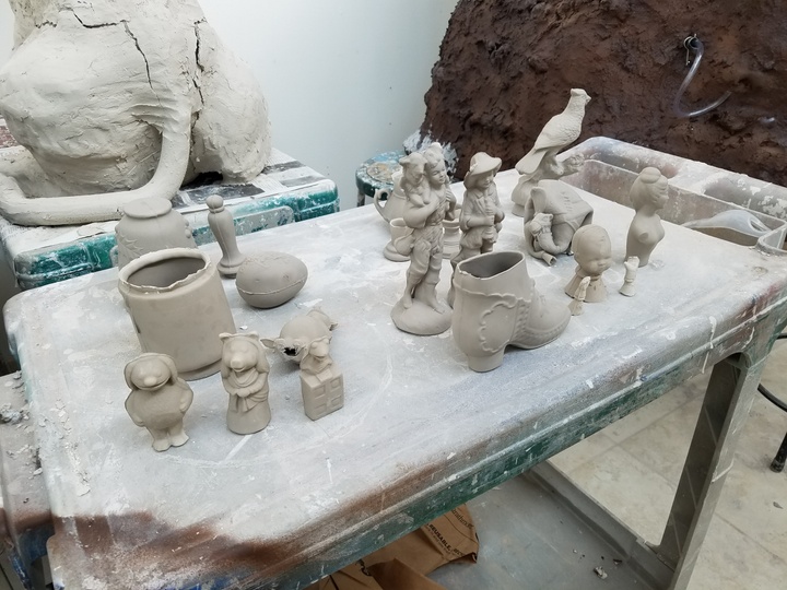 Table of a dozen small objects such as a bird statuette, a Muppet figurine, and a boot-shaped vase that have been cast in ceramic.