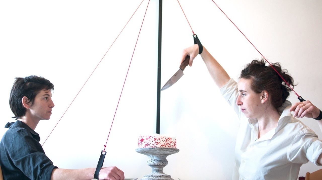 Studio Mela Two people, one holding a knife, and a cake on a cake stand.