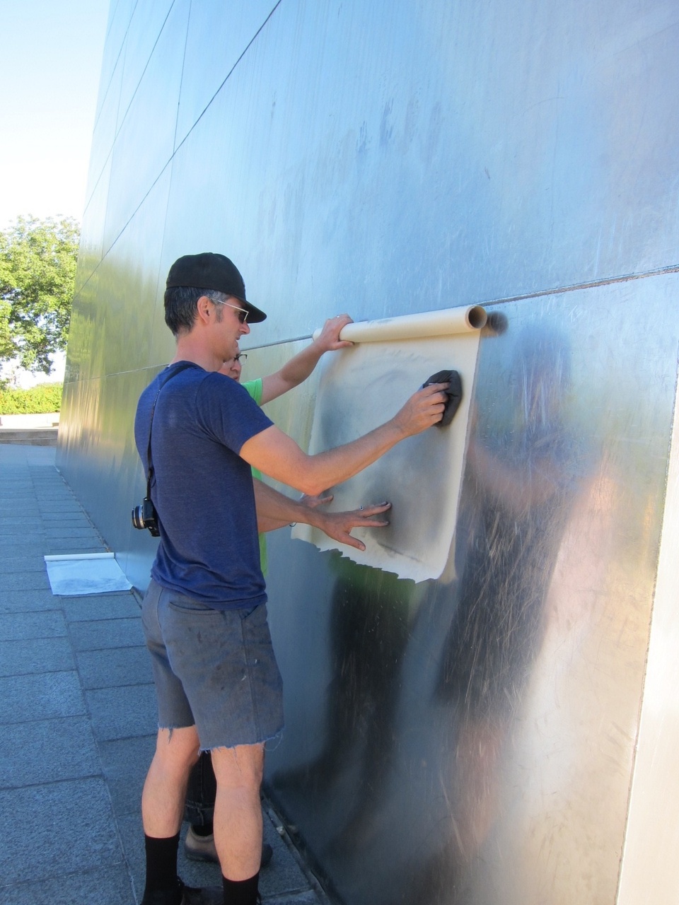 Shaun placing a large sheet of paper flat by the side of a building while rubbing a bunched up cloth over it