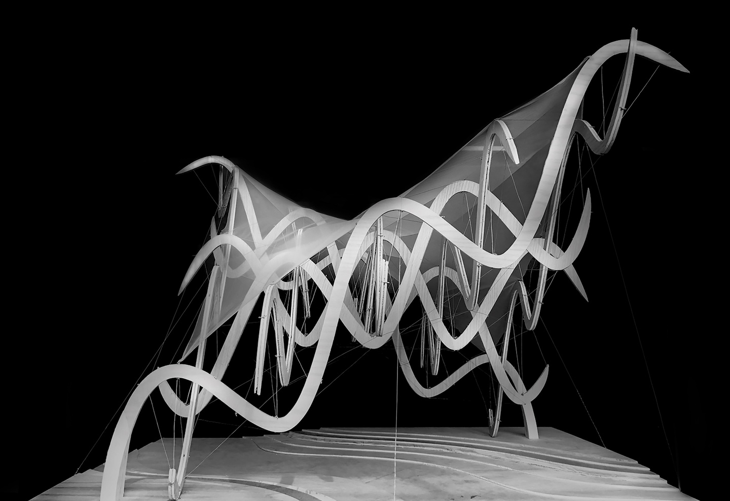 Black and white photo, showing wavy structures of an architectural model with a thin covering over them, set against a black background.