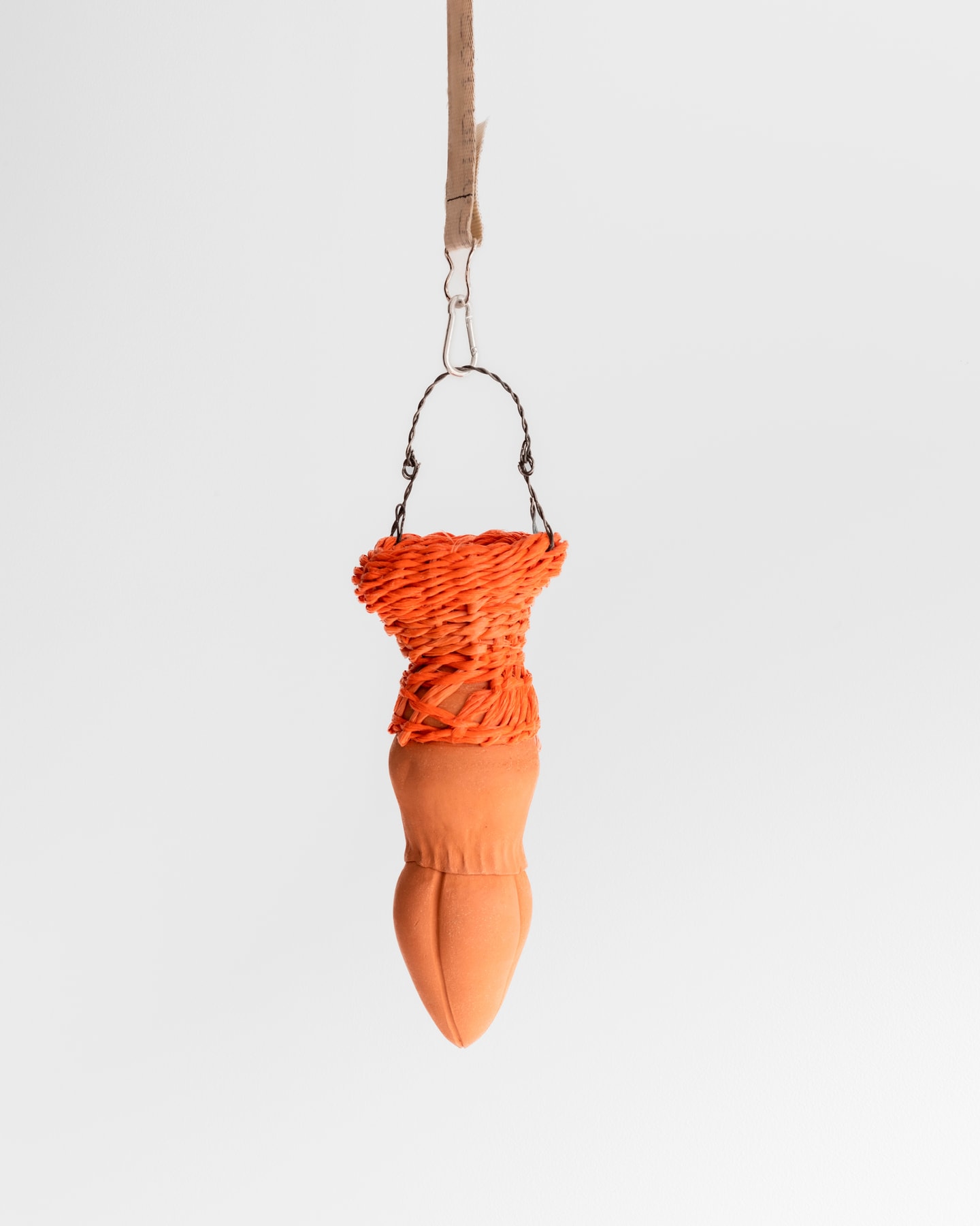 scupture of a hanging object with a cord, woven basket and ceramics in orange, terracotta and tan