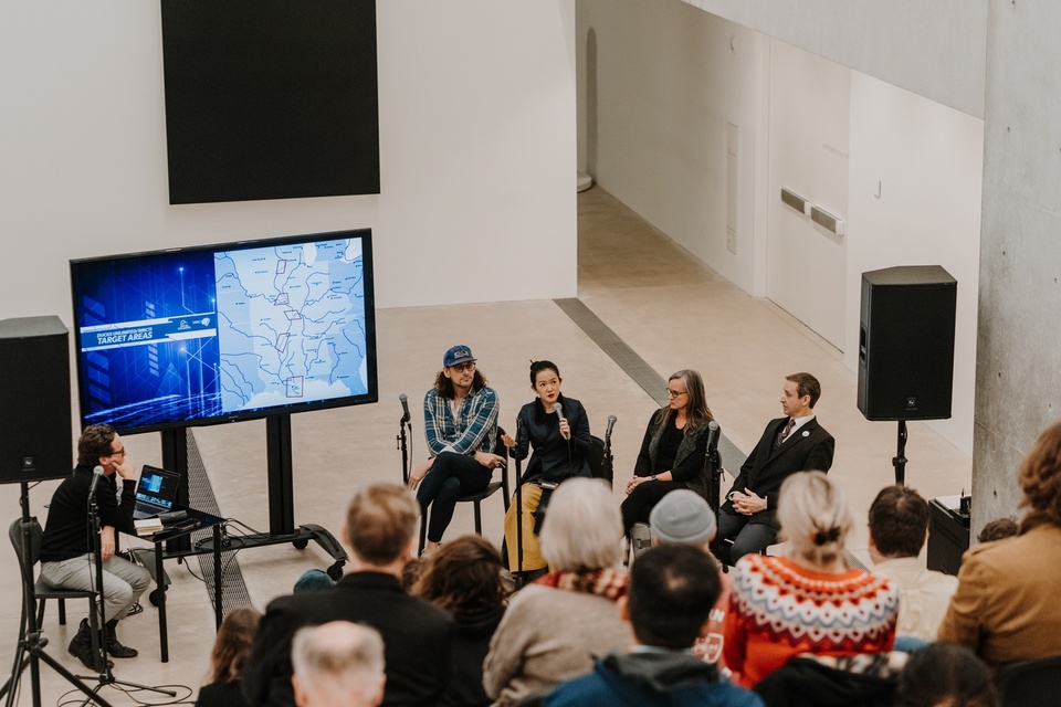 Wide shot of five panelists and crowd seated on tiered steps.