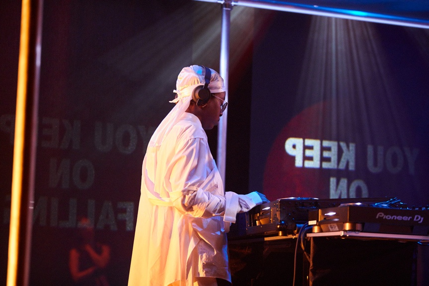 DJ in all white clothing under strobe lights.