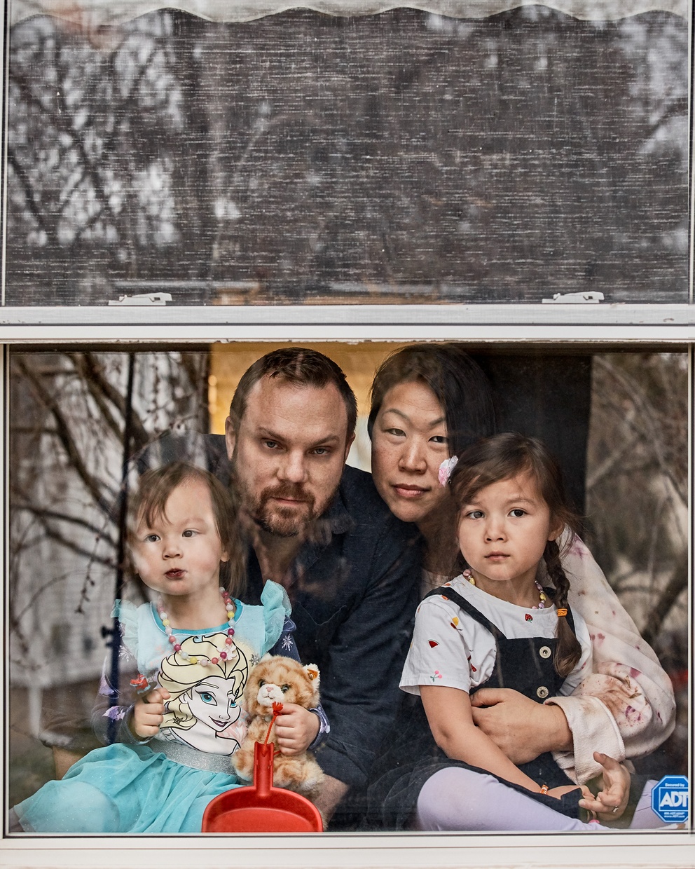 A photograph of a window with a family of four sitting behind it looking out.