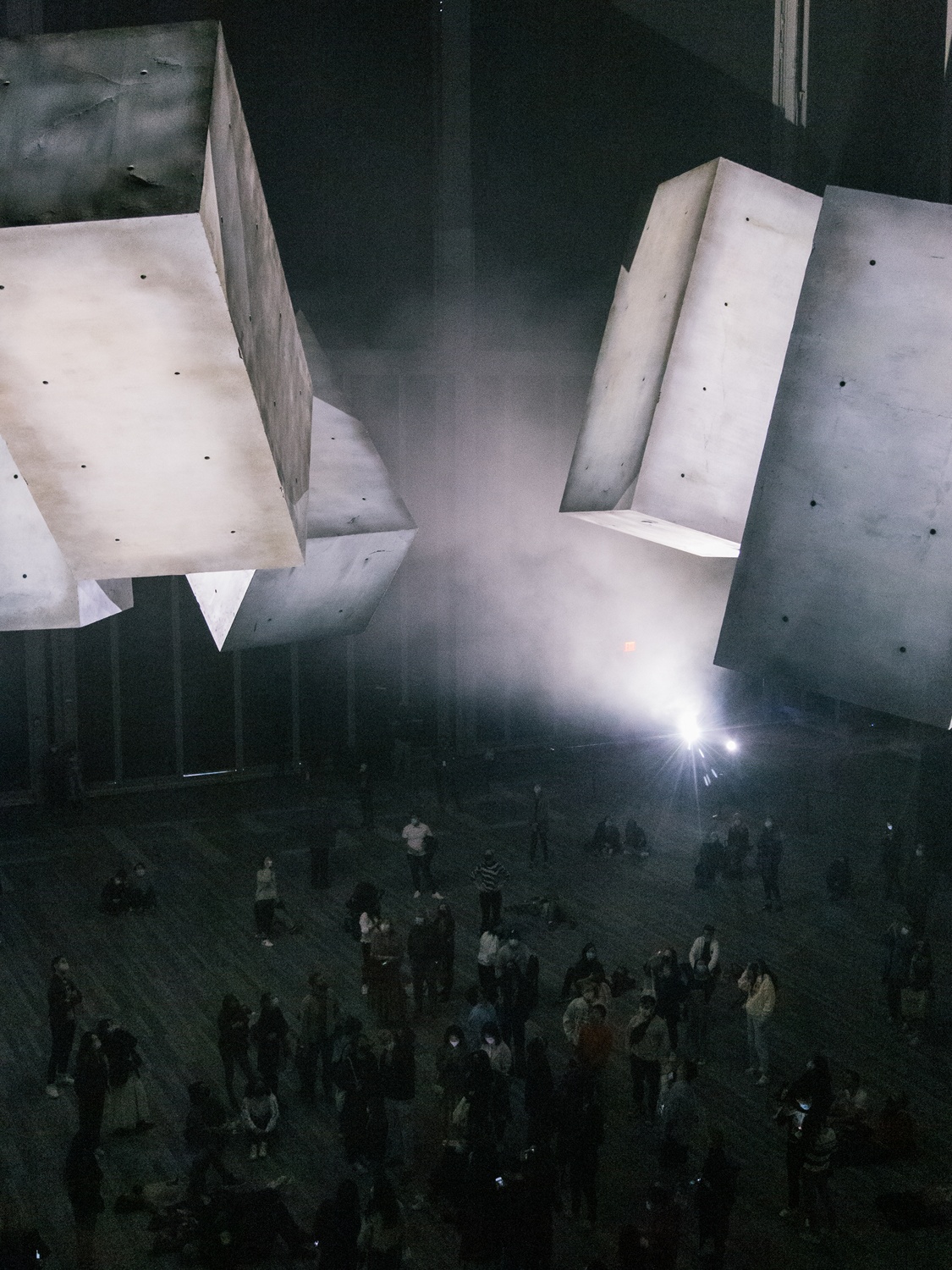 Five rectangular blocks that seem to be made of concrete float in the air above a crowd gathered beneath them