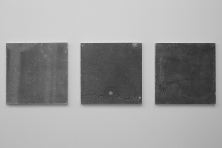 Three square, gray canvases, increasingly darker and with slight modulations from left to right