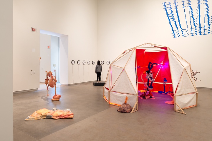 Overview shot of a gallery space with geodesic tent, sculptural works, and large-scale lettering on the wall.