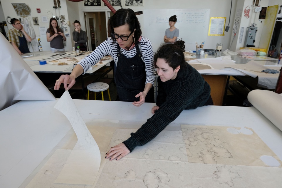 The artist lifts the paper from the plate with help from a student