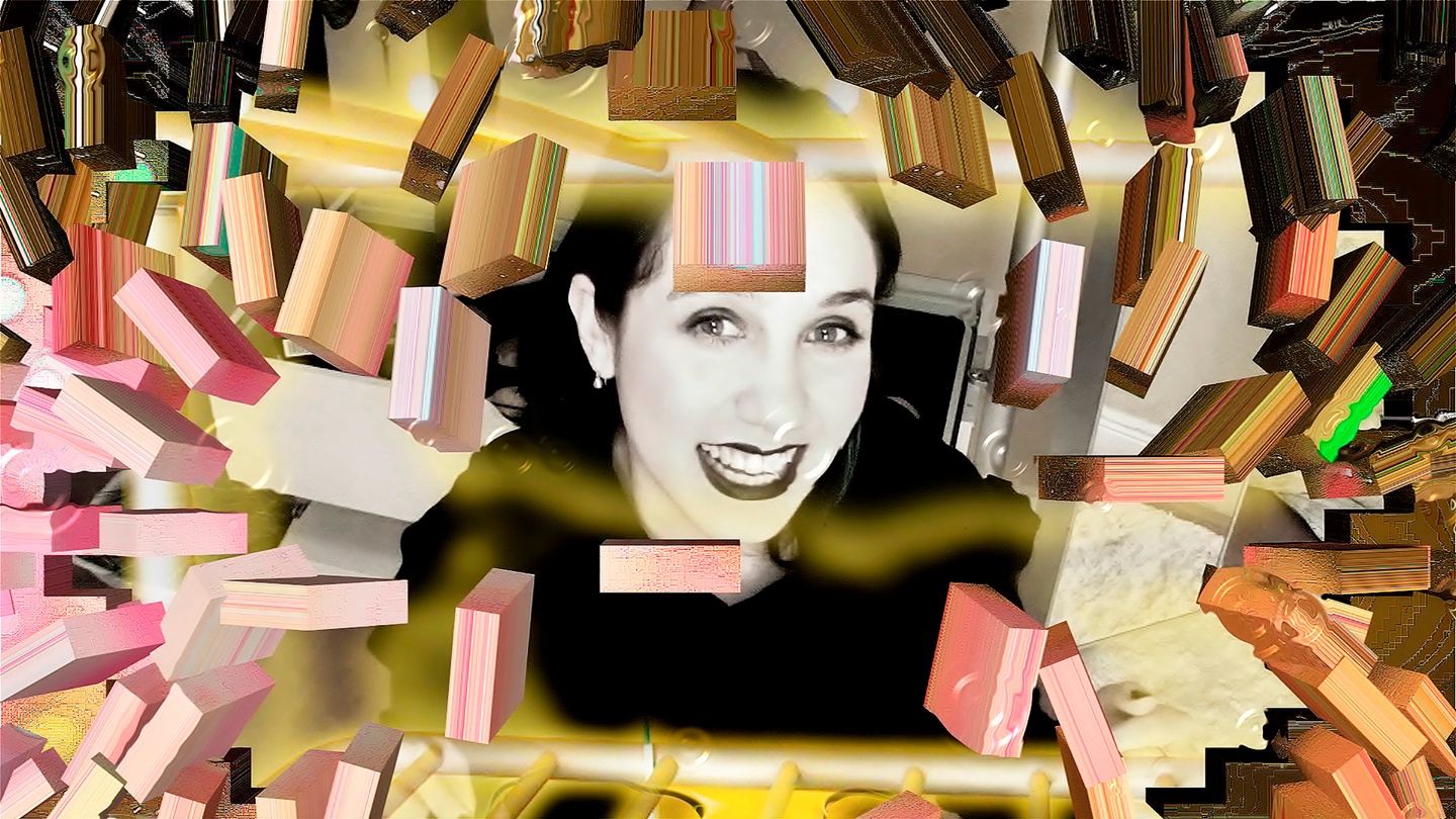 Video still; in the center is the black-and-white image of a smiling person, surrounded by 3-D blocks of pink, yellow, and brown.