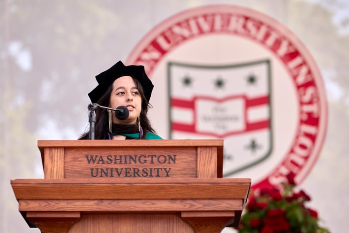 A woman wearing regalia delivers a speech from a lectern
