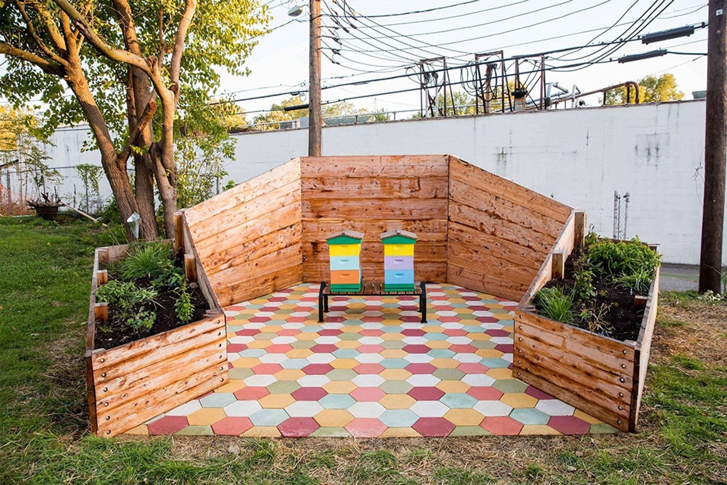 Beehives painted in bright colors on a bench, which is placed in the center of the tiled floor and surrounded by wood panels with plants to the sides. The tiling and panels both resemble beehives.