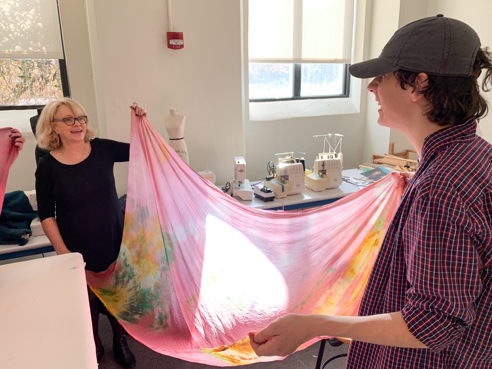 Two people stretch a piece of finished pink shibori dyed fabric out.