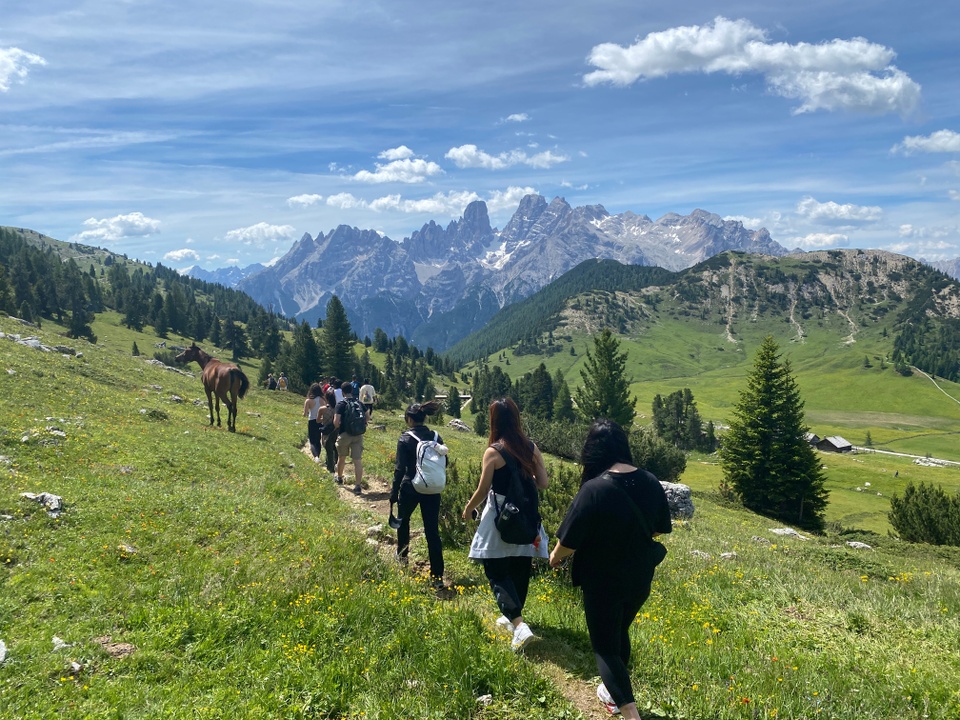 students hiking in a line on a trail in the Dolomotes mountains. lush green grass, blue sky.