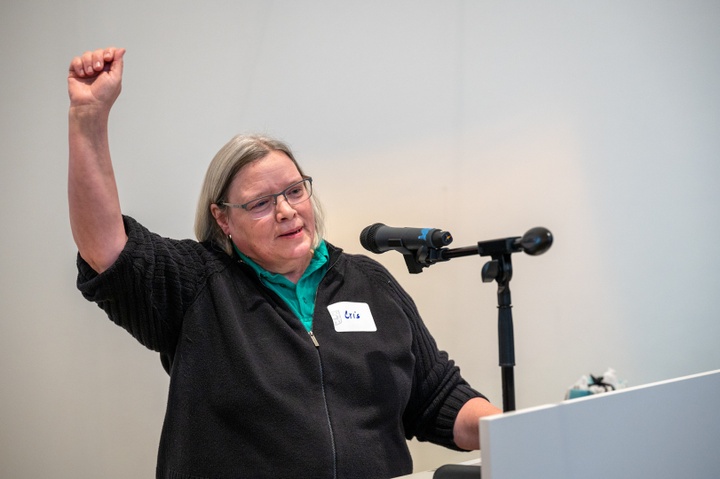 Speaker Cris Baldwin raises her right arm in a fist-pump from the lecturn.