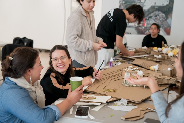 Instructor Mabe holds a cup while observing students working on a large cardboard architectural model