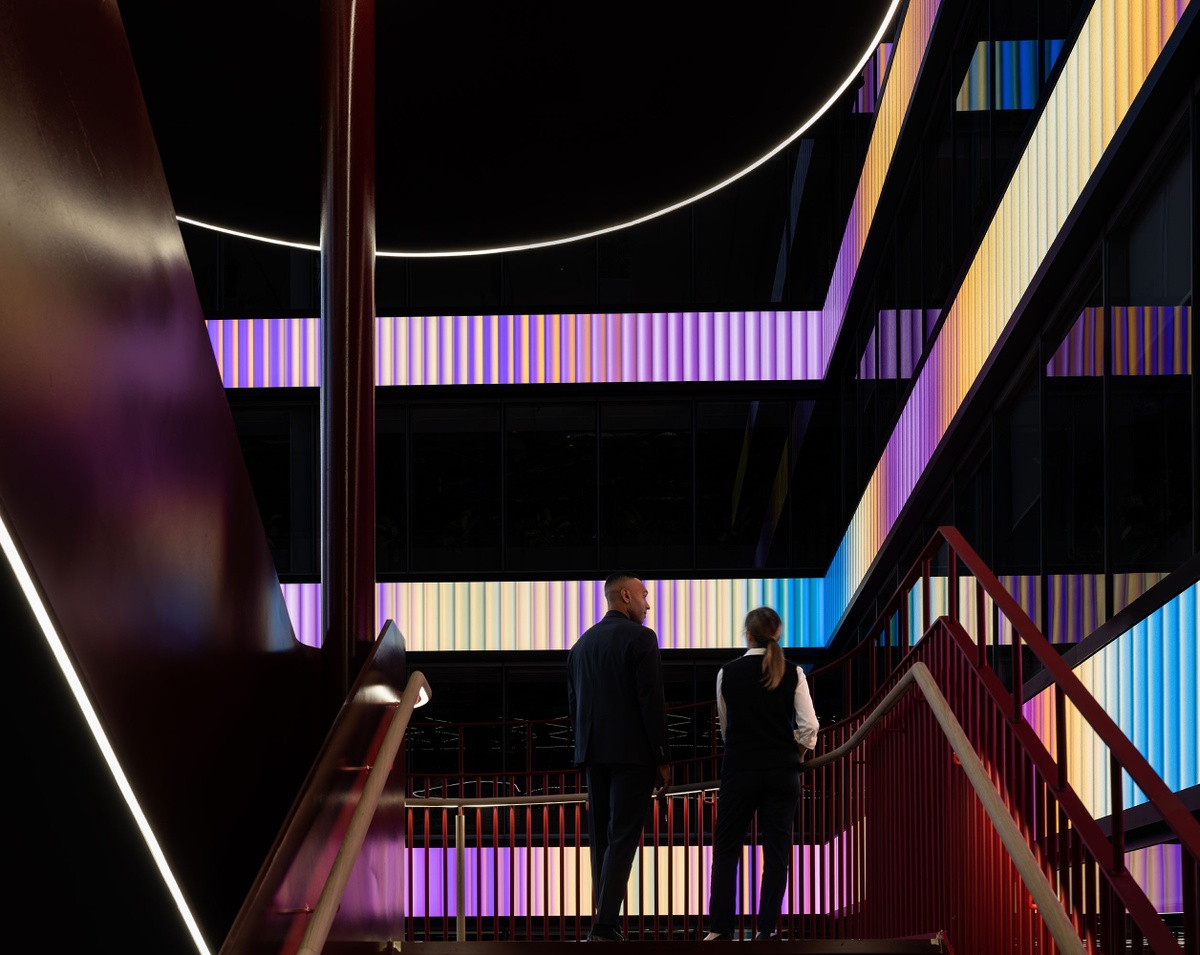 A man and woman standing on the stairwell, back lit by light from the LED screens and facing outward