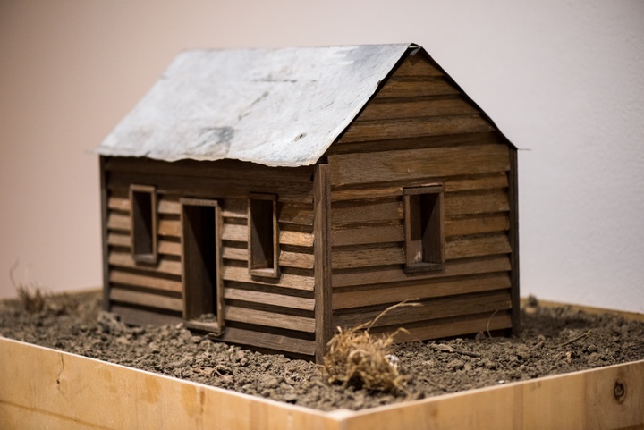Model of a wooden cabin on a bed of dirt and scrub.