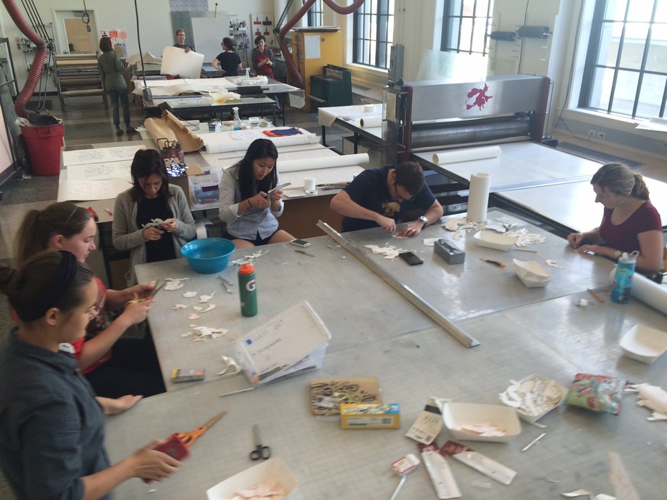 Students working with artist to cut out individual collage elements, sitting around large table in print shop