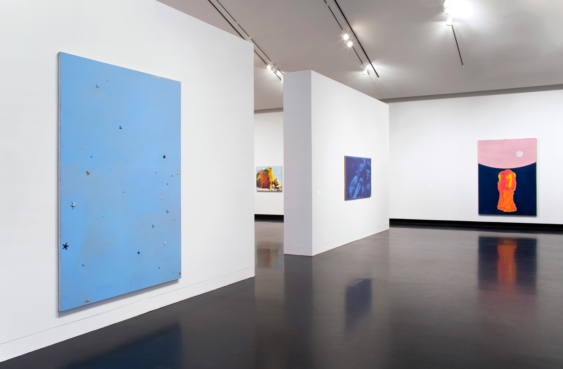 Three, large, abstract paintings on white walls. The closest painting is all blue with starfish attached to it, the painting next to it is an abstract blue painting, and the furthest painting depicts a hunched, female figure on an abstract background.