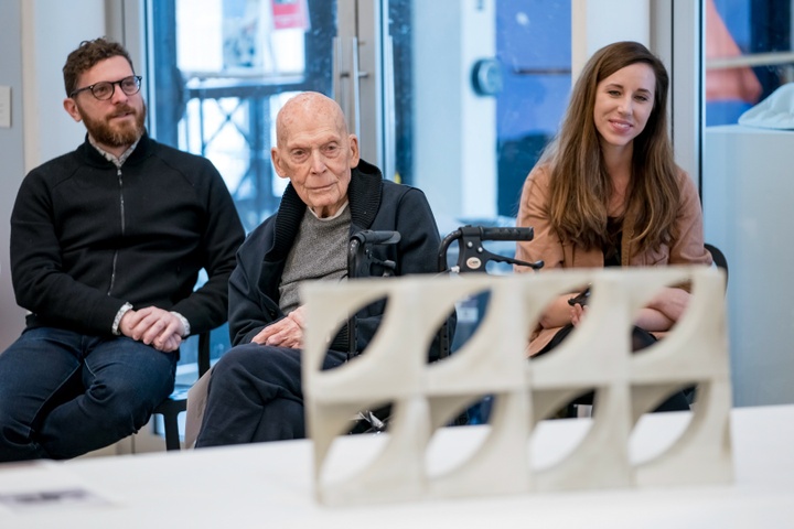 Three judges sit behind a table with modular concrete blocks piled on it.