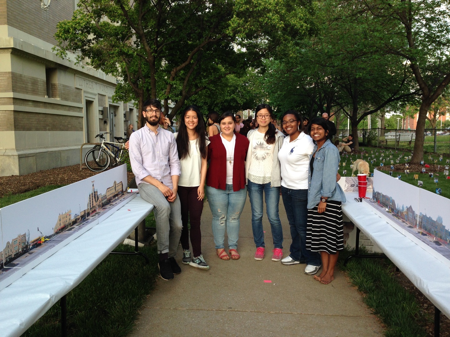 A group of six people stand between two tables in an outdoor space.