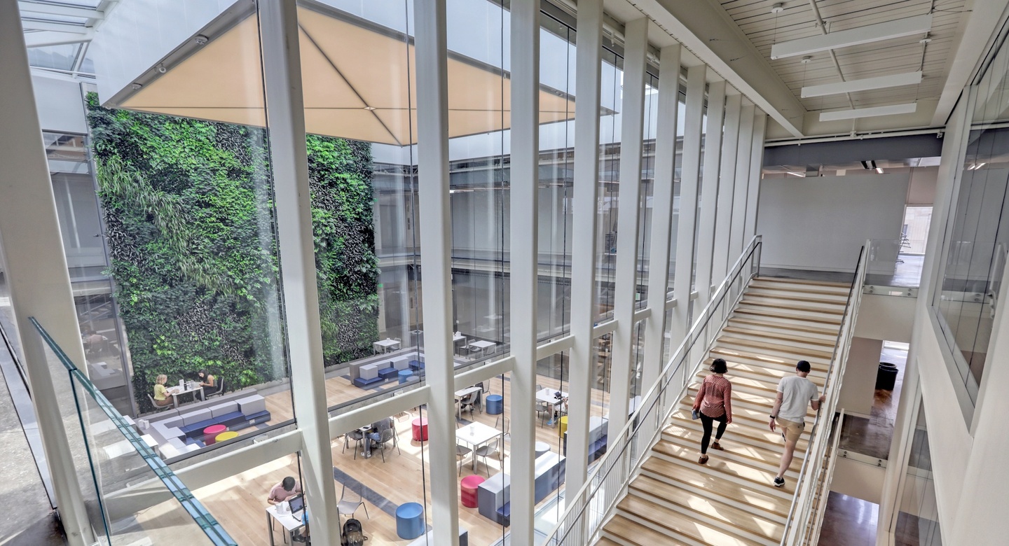 Two students acsend a wide, wood staircase overlooking a sunny interior courtyard. 