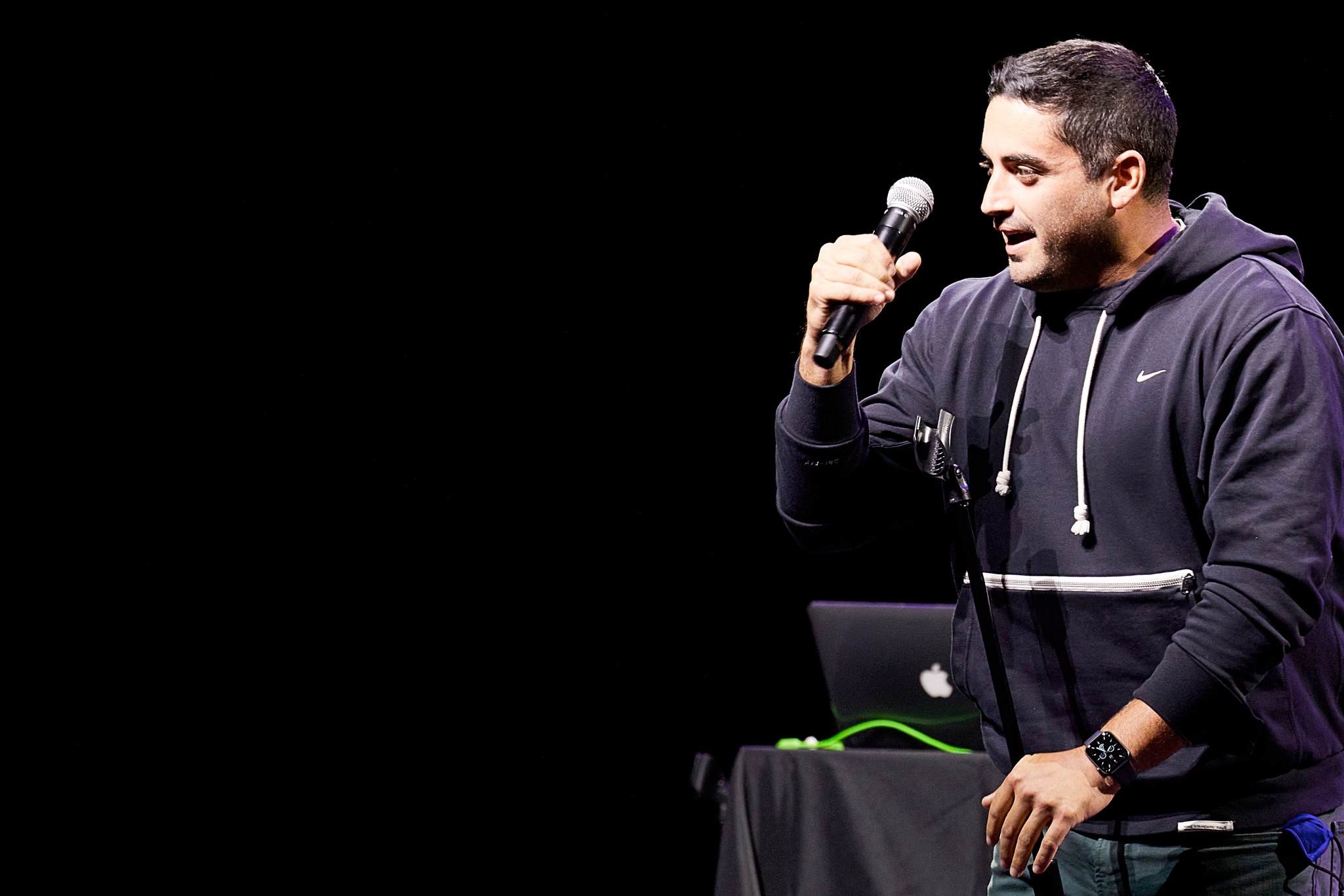 A white man in a black hoodie with a small Nike logo on the chest take a microphone off of its stand