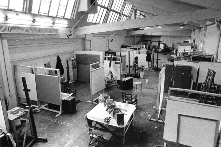 Black and white photo of an overhead view of a large studio space filled with artists' cubicles. An angled skylight along one side of the room fills the room with natural light.