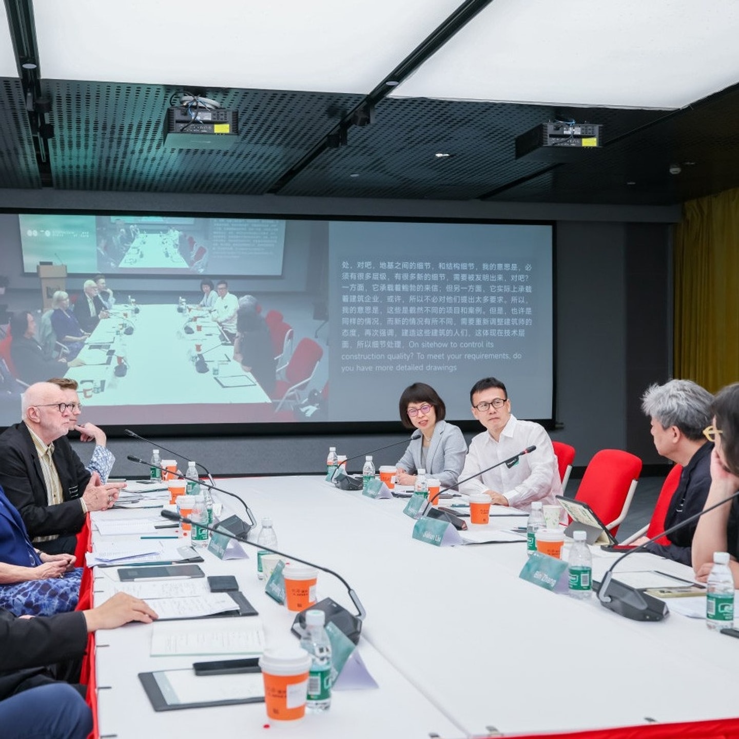 A group of people sit at a conference table with a presentation projected behind them.