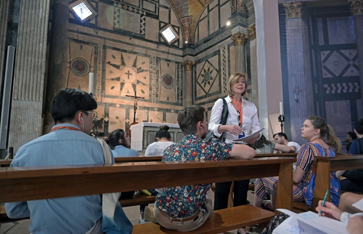 Students sit in pews in an elaborately decorated cathedral while and instructor talks.