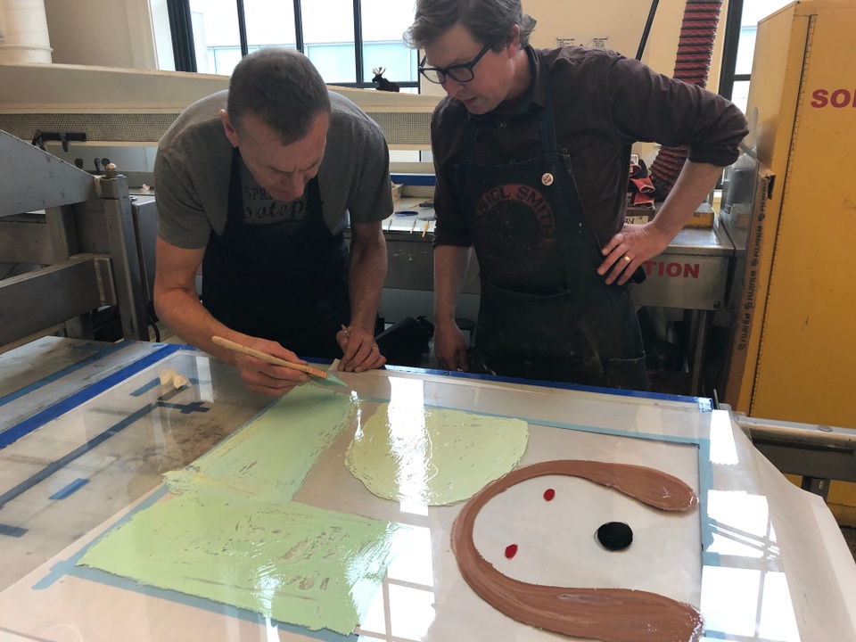 David adding pastel green details onto the transparent sheet with a large brush while Tom Reed looks on 