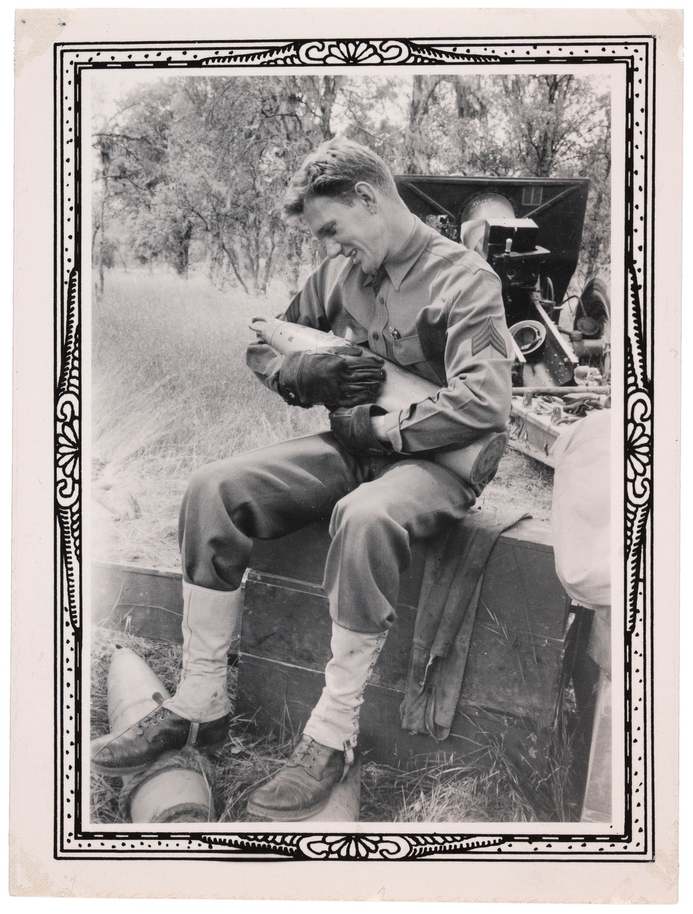 A black and white photograph of a seated man in military uniform and gloves cradling and looking down happily at a missile.