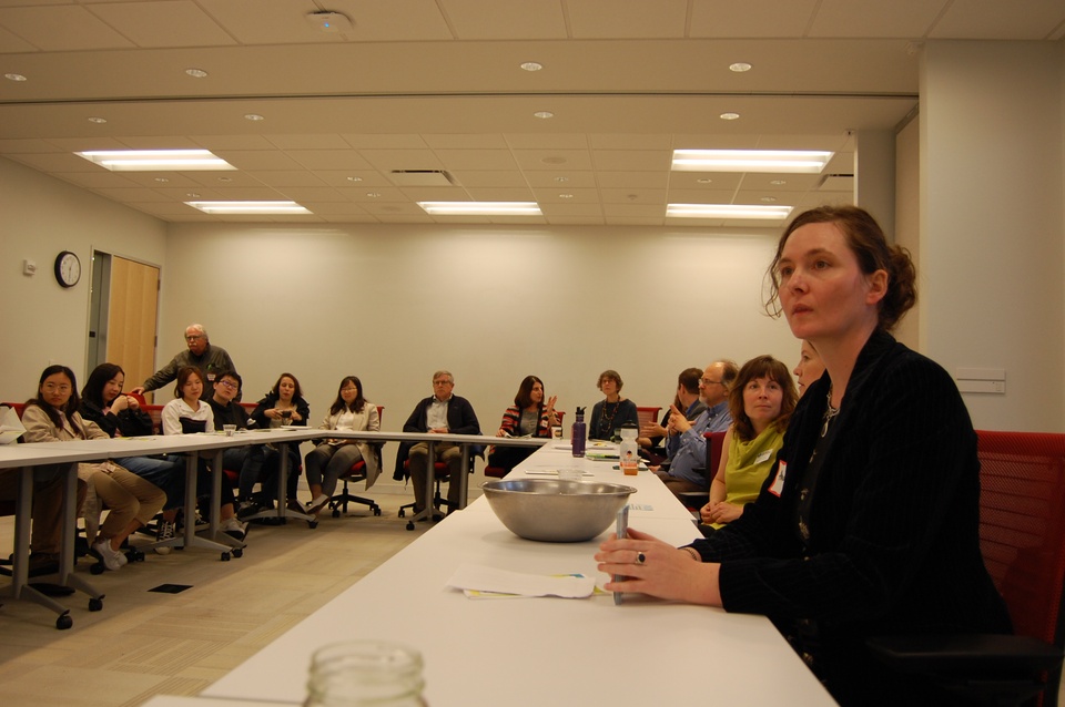 People sit around a table, with one person in the foreground speaking. 