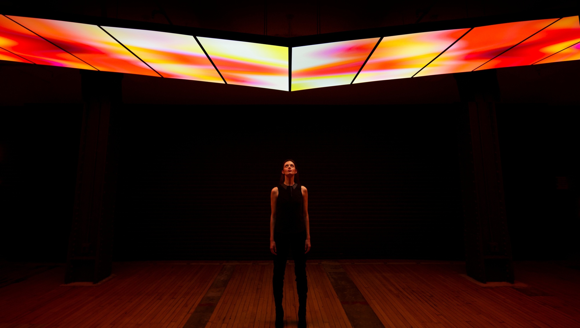 Symmetrical image of a woman looking up at The Skywalk structure, which dips in the center, and glows with a mesmerizing white, red and yellow gradient