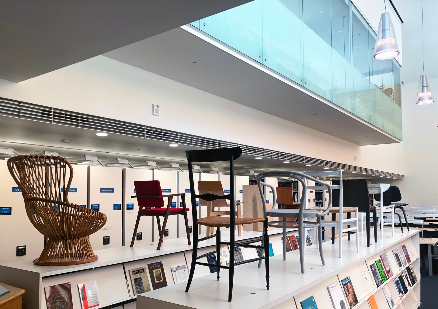 Exhibition of several architectural chairs, displayed atop a pair of magazine shelving units in the library.