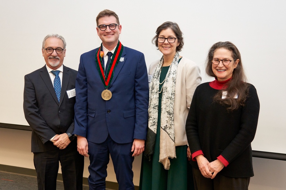 Four people, one with a medallion around his neck, stand next to each other.