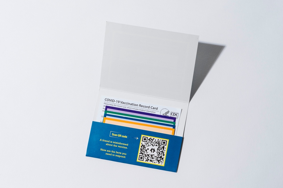 One card holder lies open on the surface, with four conversation cards and a vaccination card tucked in. There is a QR code, along with some text that reads "Scan QR code. A friend is misinformed about the vaccine. Here are the facts you need to respond."