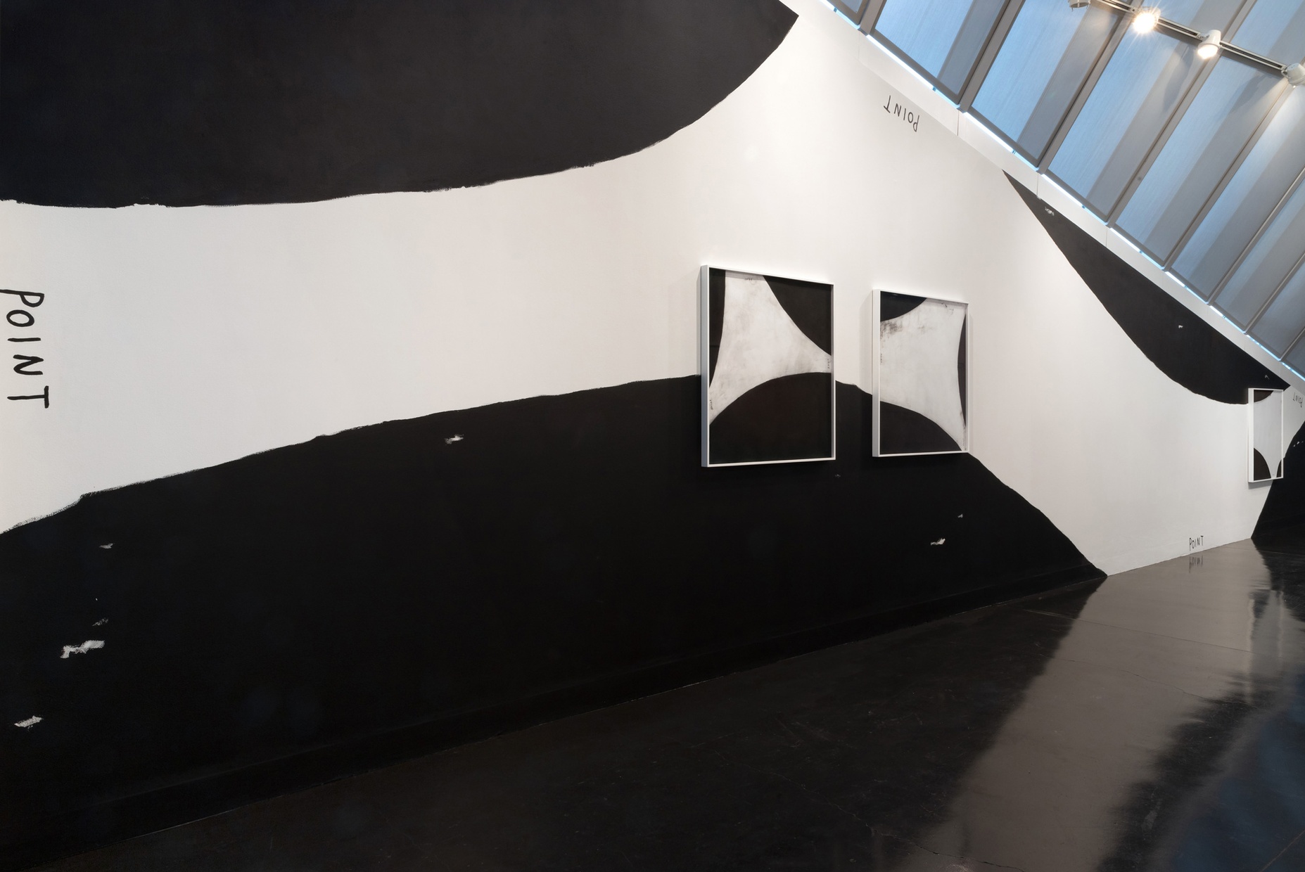 A wall painted in sections of black and white with similar black and white sections framed, hanging on top of the mural.