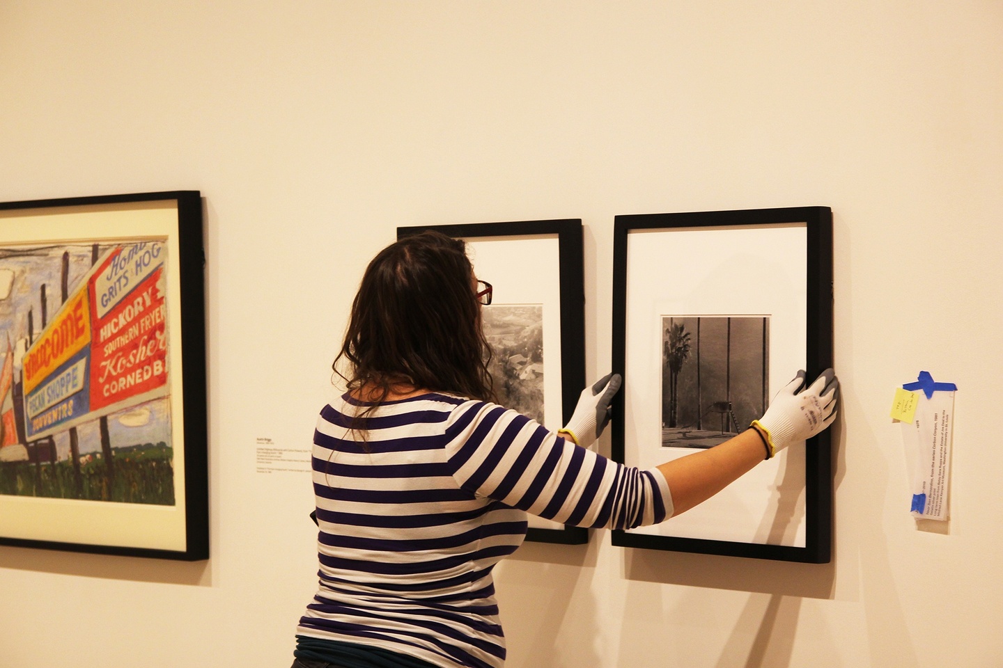 A person hanging a framed black-and-white photo on a wall with two other framed artworks