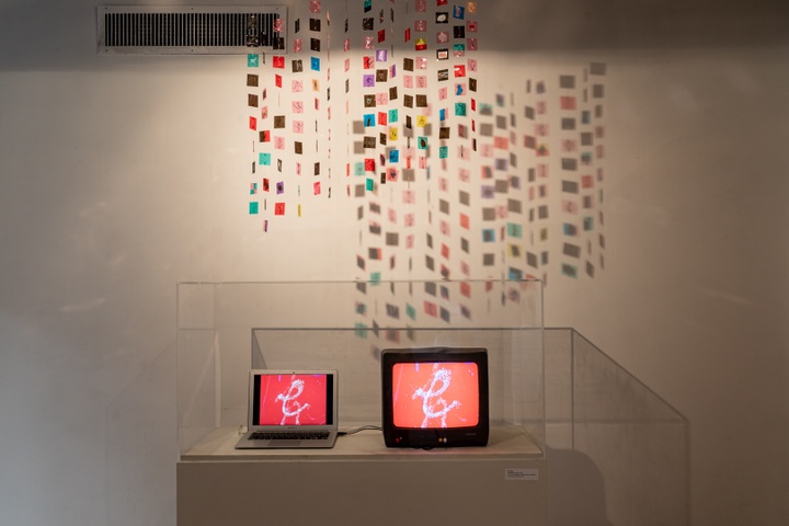 Small tv connected to a laptop displays a red graphic. Hanging behind it is a moble of small colored plastic squares.