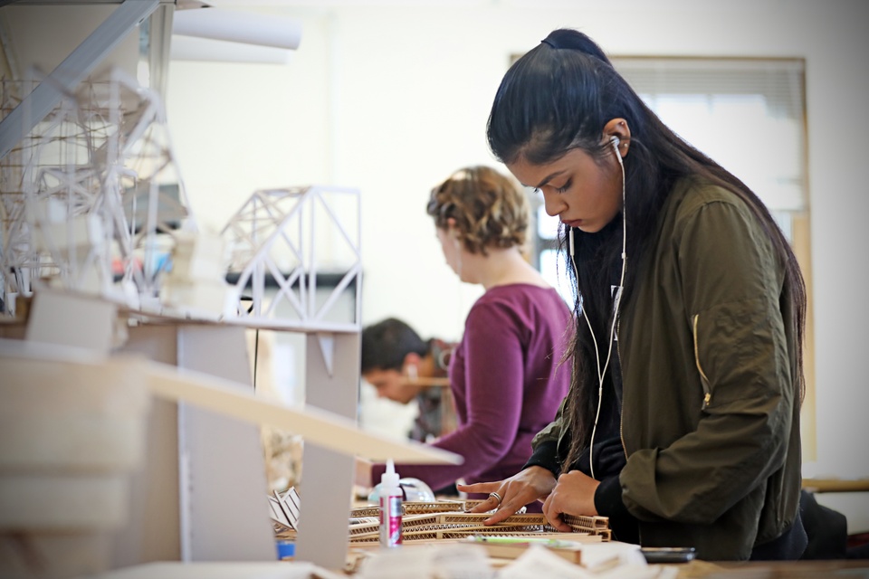 Line of students at worktables glueing and assembling basswood models of bridges.