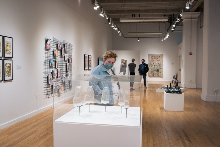 View of several people looking around a gallery space with sculptural and 2D works.