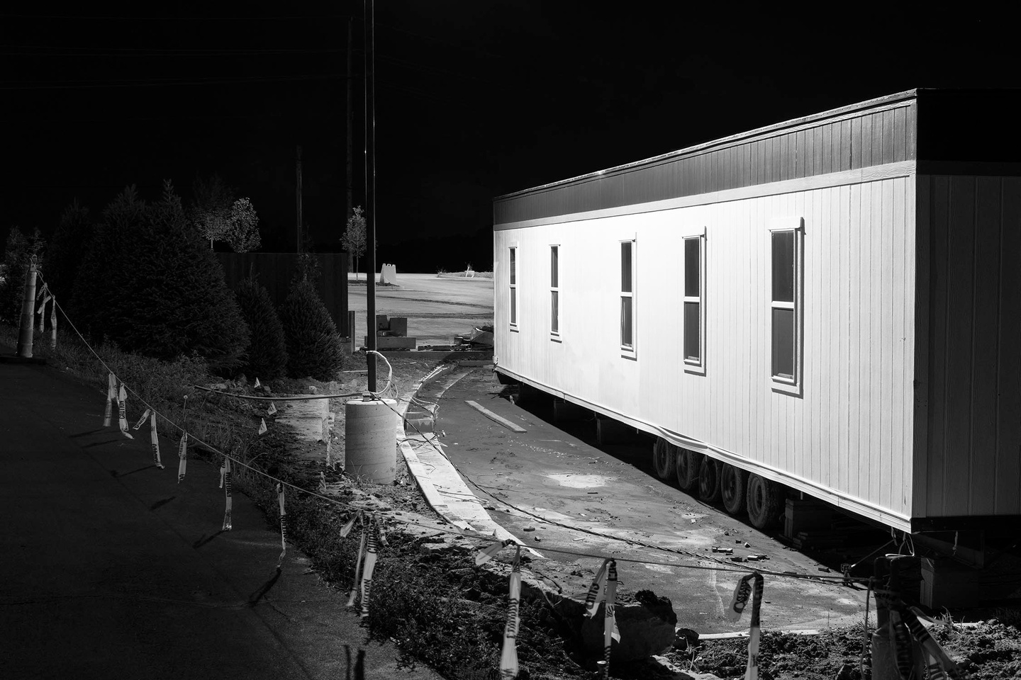 Black and white photo showing a trailer lit by a bright light, with a wire fence to the left.