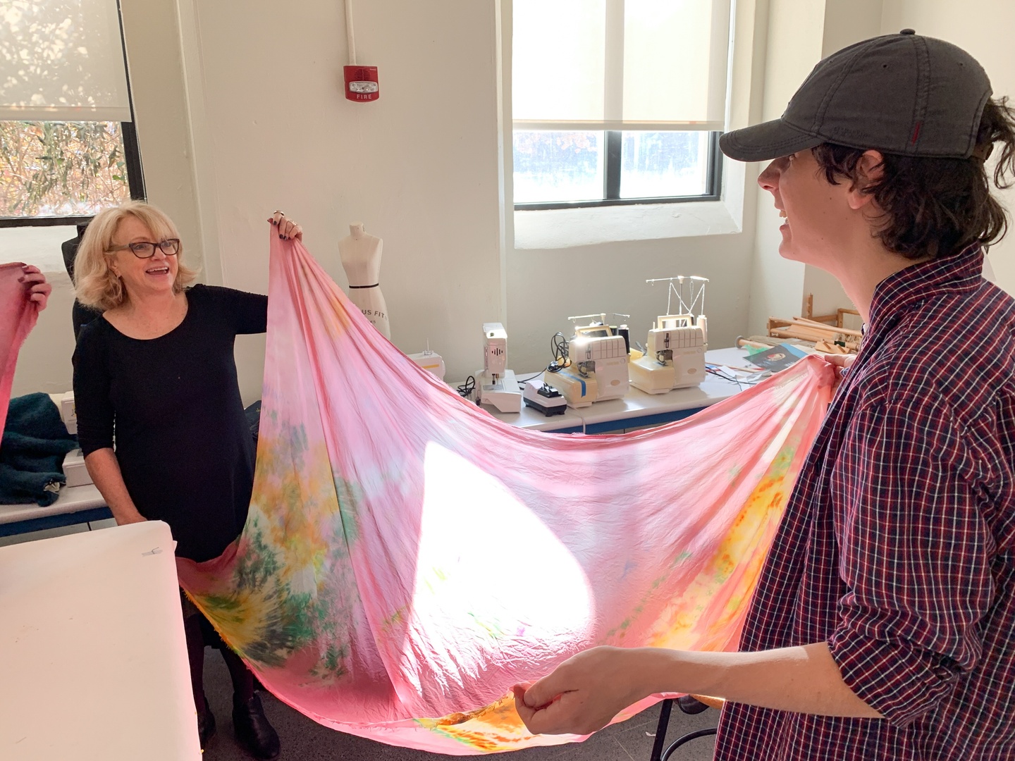 Two smiling people spread out opposite corners of a hand-dyed sheet.