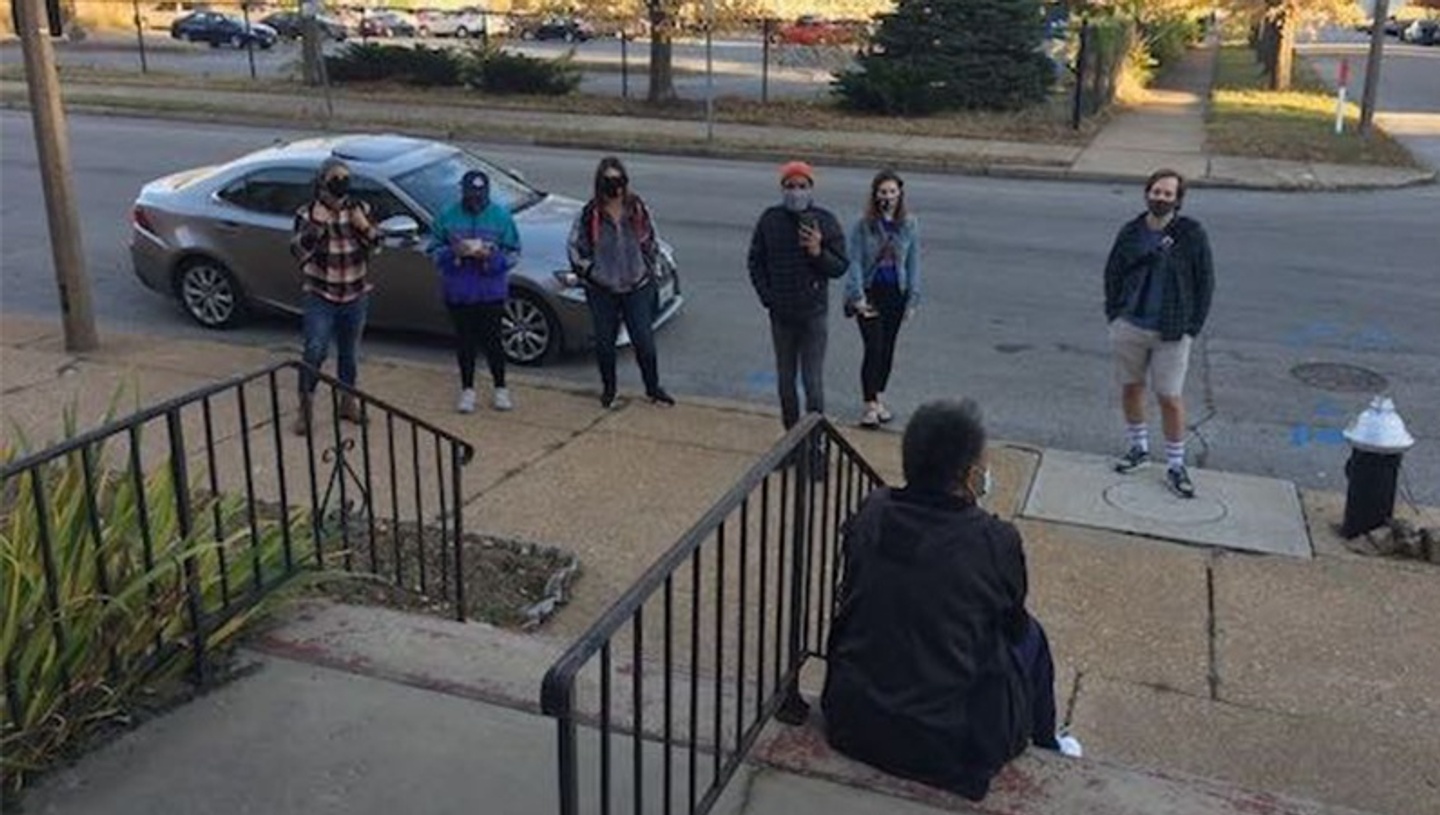 A group of people look at a person sitting on a set of stairs outside a building. 