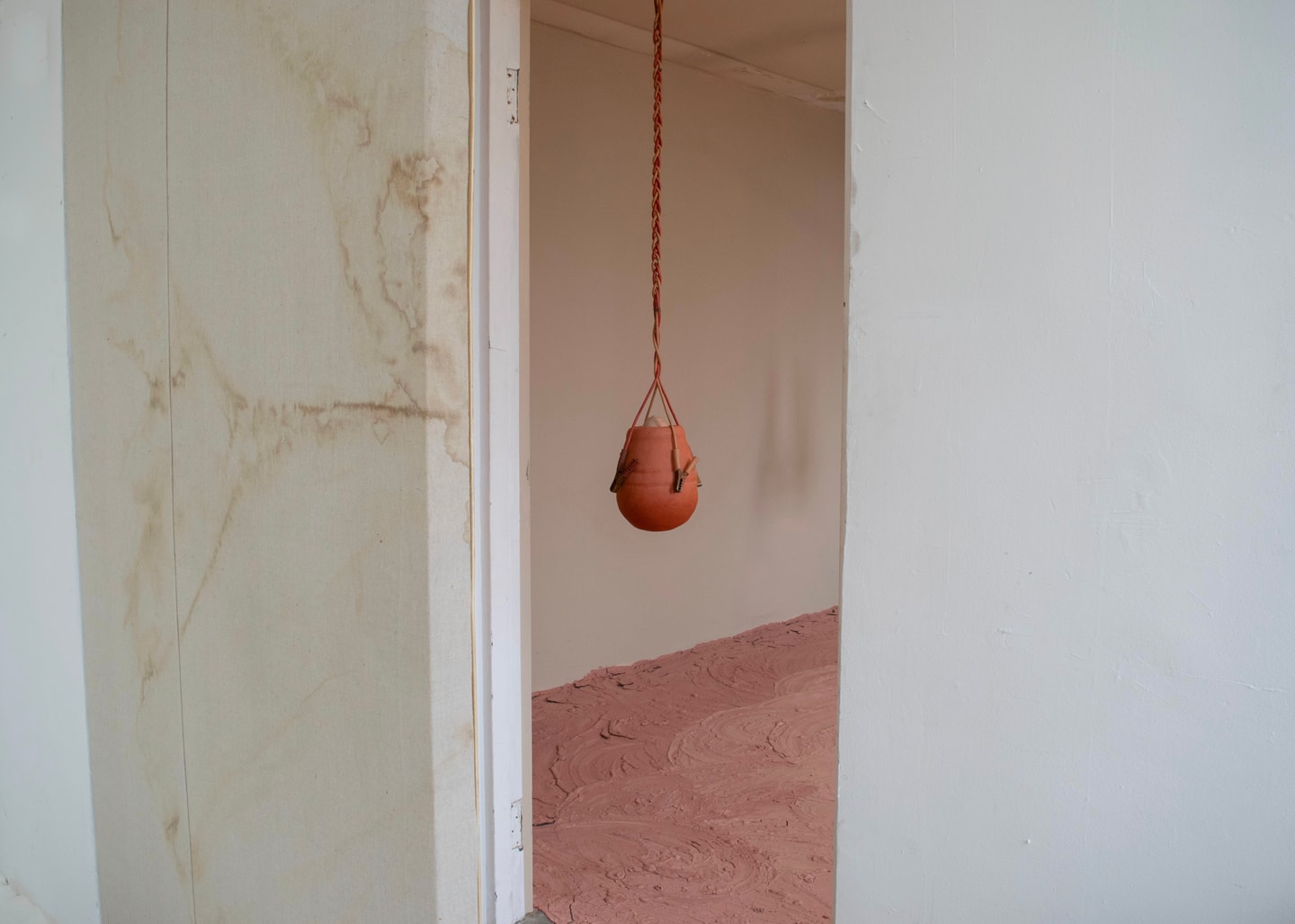 installation view in a gallery of a sculpture of a hanging jar made from ceramics in terracotta, reds, and tans