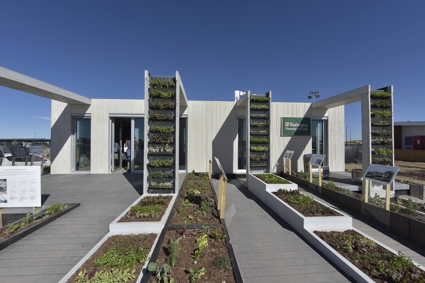 Boxy concrete single-story house with four projecting buttresses that serve as vertical gardens. The house is set on a very large deck filled with rows of garden boxes.