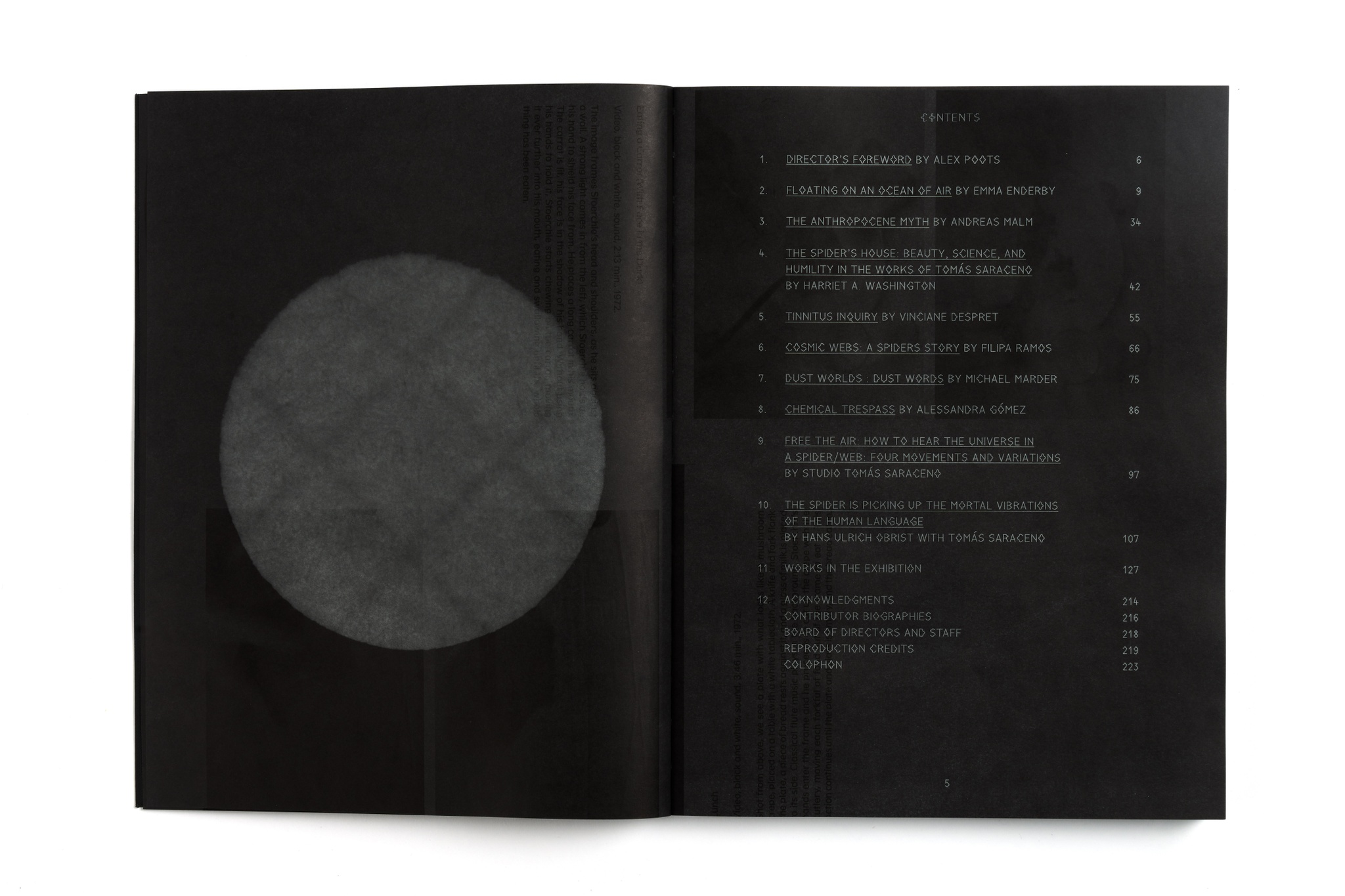 An exhibition catalogue lying open on a white surface. The book has black pages and its table of contents is listed in silvery text.