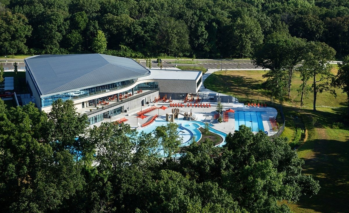 Aerial photo of a community center with an outdoor pool plus lazy river area, with green trees in the foreground.
